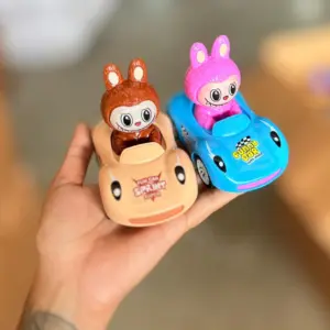 Carritos de fricción Labubu sostenidos en una mano: uno beige con figura café y otro azul con figura rosa, mostrando su tamaño compacto.